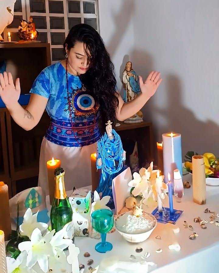 Mãe Ana de Iemanjá em oração diante do altar com velas, flores e a imagem de Iemanjá